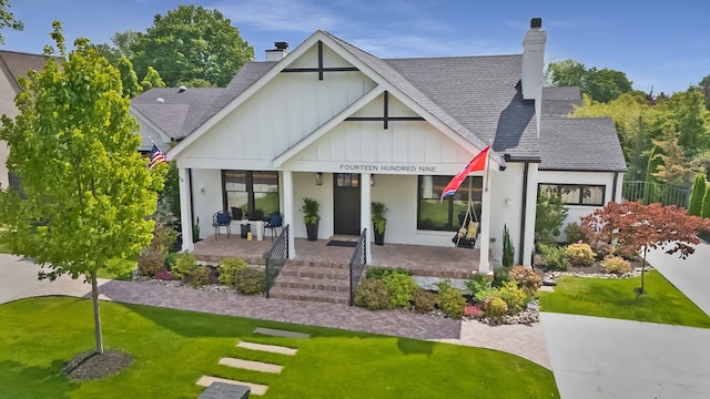 rear view of house featuring a porch, a lawn, a chimney, and roof with shingles