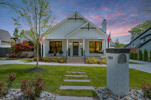 view of front facade with board and batten siding, a chimney, covered porch, and a front lawn