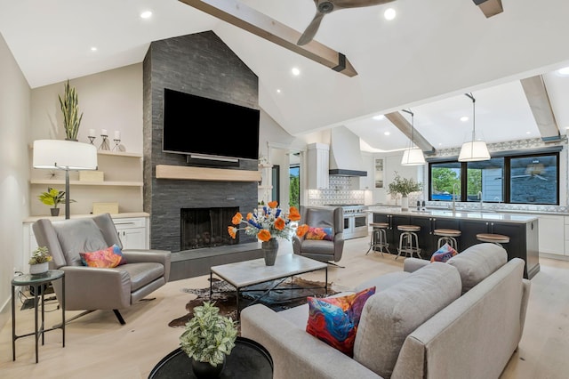 living area featuring vaulted ceiling with beams, ceiling fan, a fireplace, and light wood-type flooring