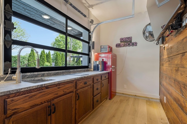 kitchen featuring light wood-type flooring, a sink, brown cabinetry, and baseboards
