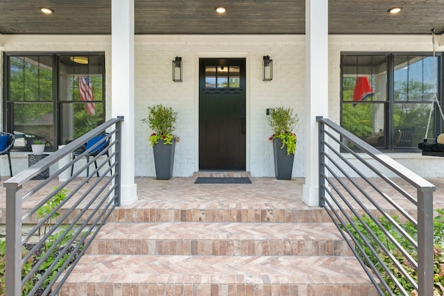 view of exterior entry with a porch and brick siding