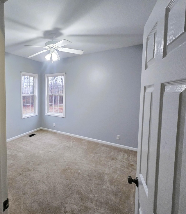 carpeted empty room with visible vents, a ceiling fan, and baseboards