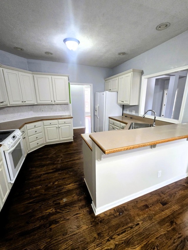 kitchen featuring a textured ceiling, dark wood finished floors, a sink, a peninsula, and white appliances