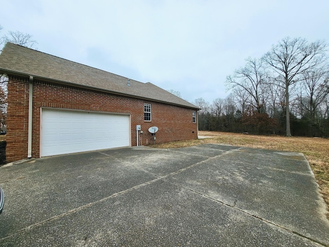 view of side of property with brick siding, driveway, and roof with shingles