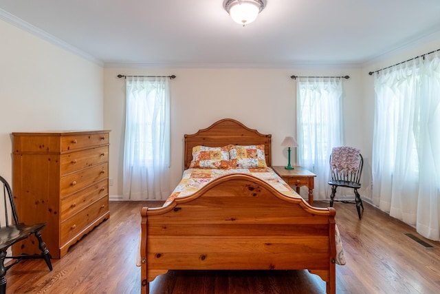 bedroom featuring baseboards, ornamental molding, light wood-type flooring, and visible vents