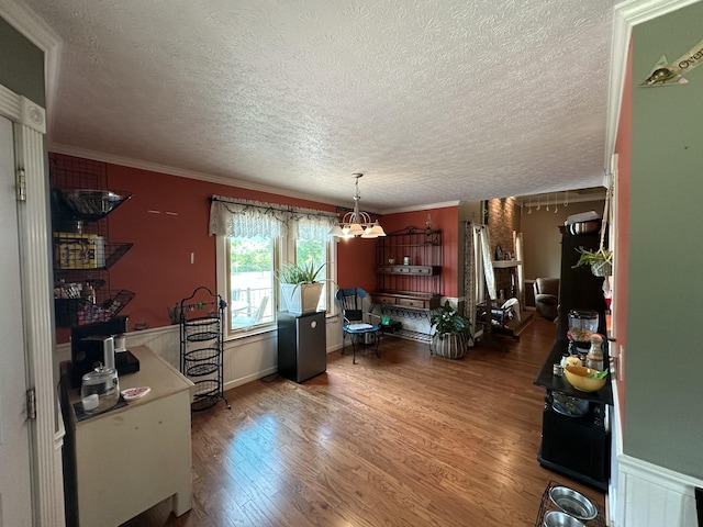 office space featuring a notable chandelier, a textured ceiling, a wainscoted wall, wood finished floors, and ornamental molding