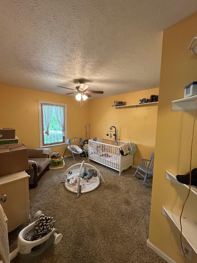 carpeted bedroom featuring a ceiling fan, a textured ceiling, a crib, and baseboards