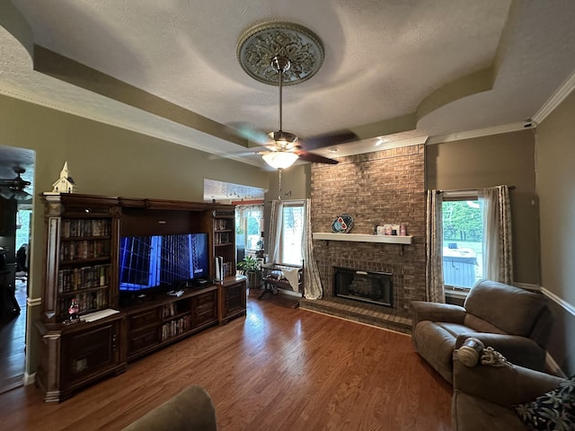 living area featuring a brick fireplace, a ceiling fan, a tray ceiling, and wood finished floors