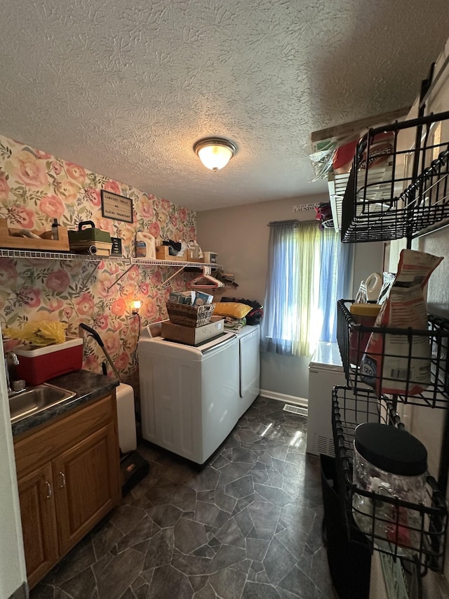 laundry area featuring stone finish floor, a textured ceiling, cabinet space, a sink, and washer and clothes dryer