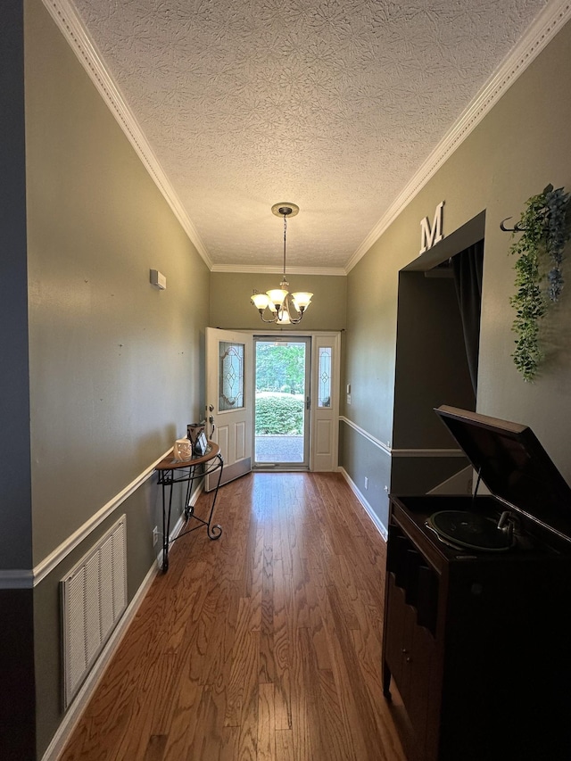 doorway to outside featuring a textured ceiling, visible vents, crown molding, wood finished floors, and a chandelier