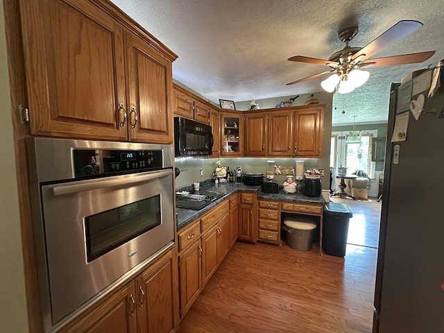 kitchen with brown cabinets, a textured ceiling, black appliances, and light wood-style floors
