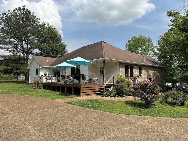 rear view of house featuring a lawn, a shingled roof, and a deck