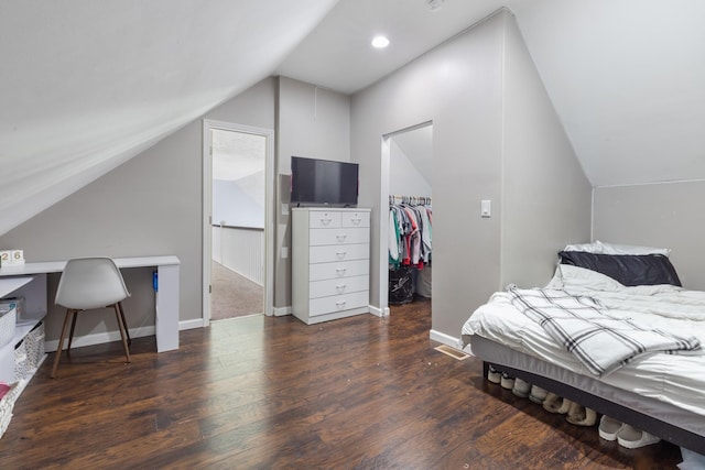 bedroom featuring a closet, wood finished floors, lofted ceiling, baseboards, and a walk in closet
