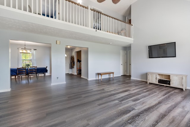 living room featuring a ceiling fan, baseboards, a high ceiling, and dark wood-type flooring