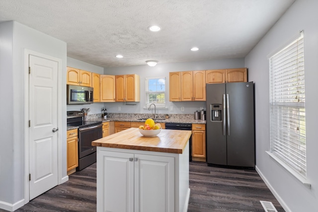 kitchen with a center island, stainless steel appliances, dark wood-type flooring, visible vents, and butcher block counters