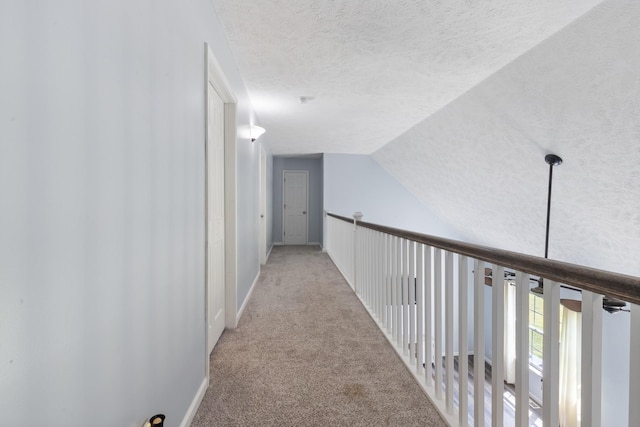 corridor featuring carpet floors, baseboards, vaulted ceiling, and a textured ceiling