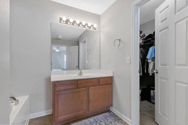 full bathroom featuring a walk in closet, ceiling fan, a bath, vanity, and baseboards