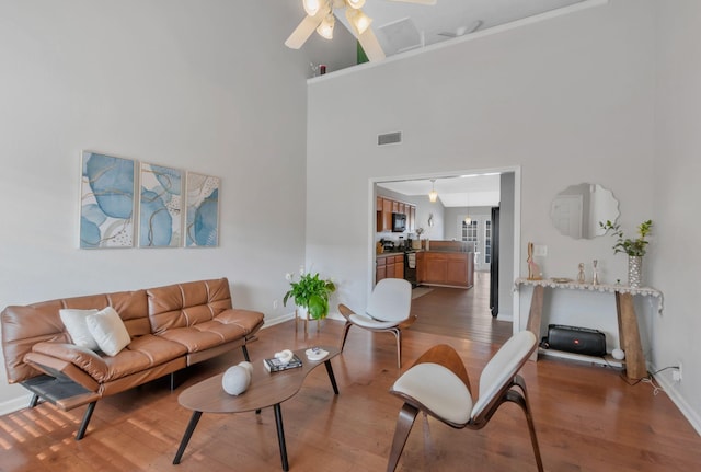 living area featuring visible vents, ceiling fan, wood finished floors, and a high ceiling