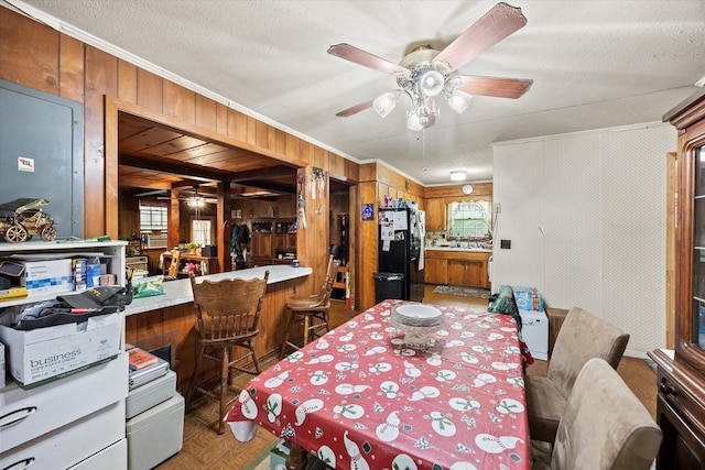 dining room with plenty of natural light, ornamental molding, a ceiling fan, and wood walls