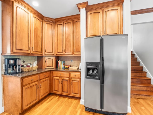 kitchen with decorative backsplash, dark stone counters, brown cabinets, stainless steel fridge with ice dispenser, and light wood finished floors
