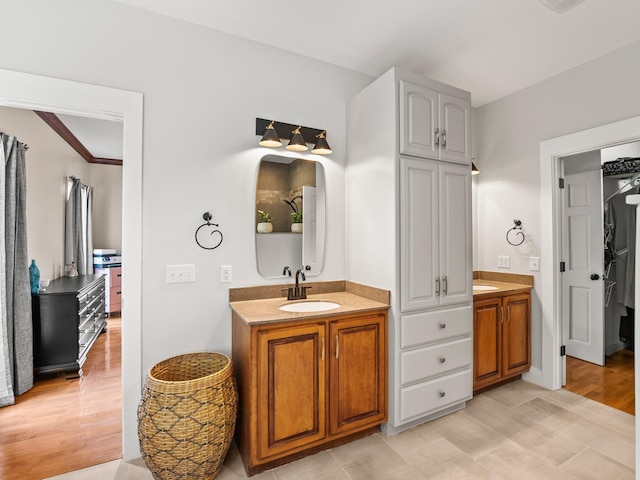 bathroom featuring wood finished floors, two vanities, a sink, and a closet