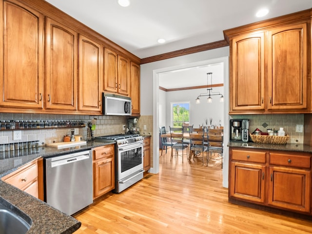 kitchen featuring brown cabinetry, ornamental molding, light wood finished floors, backsplash, and stainless steel appliances