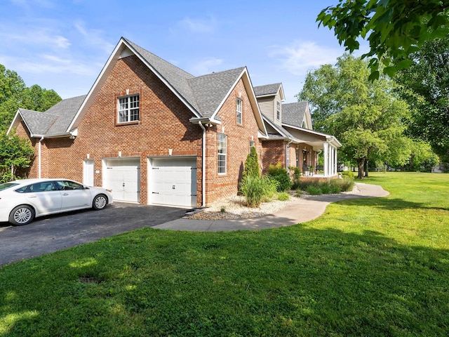 view of side of home featuring roof with shingles, an attached garage, brick siding, a yard, and driveway