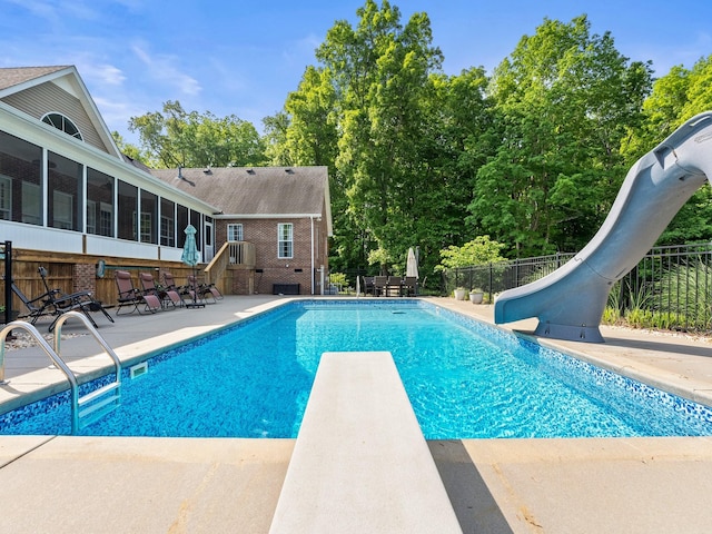 view of swimming pool with fence, a diving board, a water slide, a fenced in pool, and a patio