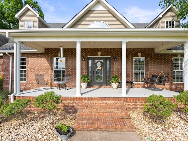 view of exterior entry featuring roof with shingles, a porch, and brick siding