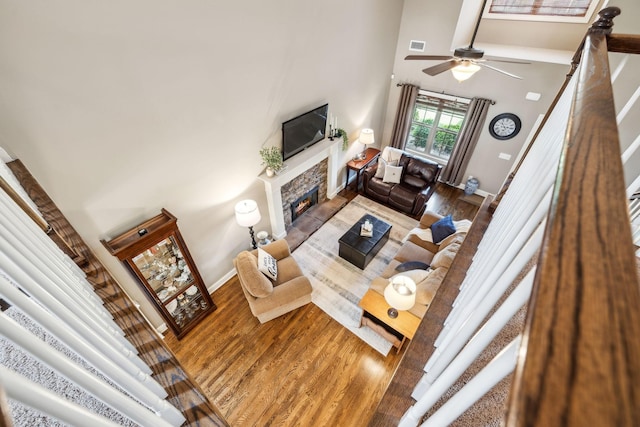 living area featuring baseboards, a high ceiling, wood finished floors, and a warm lit fireplace