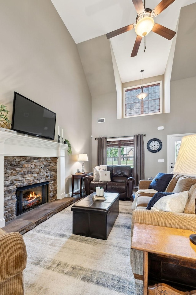 living area featuring high vaulted ceiling, visible vents, a stone fireplace, and ceiling fan