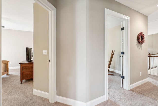 corridor featuring baseboards, an upstairs landing, and carpet