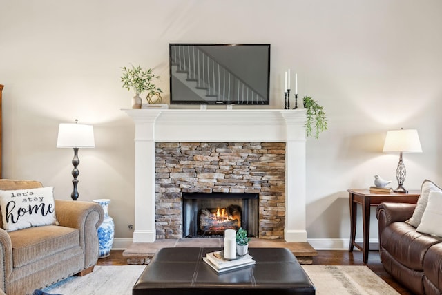living room featuring baseboards, stairs, wood finished floors, and a stone fireplace