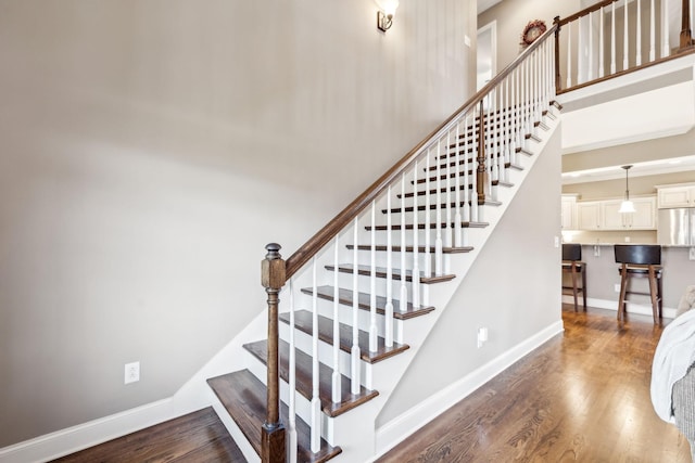 stairs with baseboards, wood finished floors, and a towering ceiling