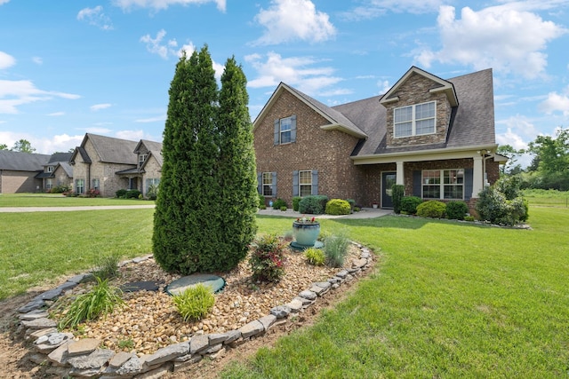 view of front of property with a shingled roof, brick siding, and a front yard