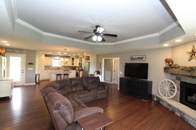 living area featuring ceiling fan, crown molding, dark wood finished floors, a raised ceiling, and recessed lighting