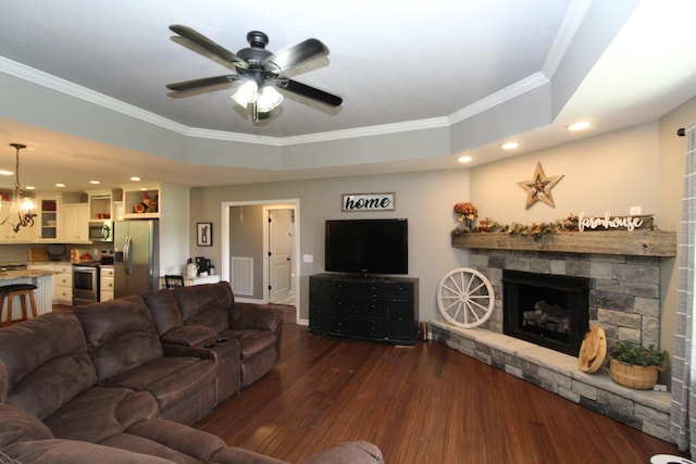 living room with ceiling fan, dark wood-style floors, ornamental molding, and a stone fireplace