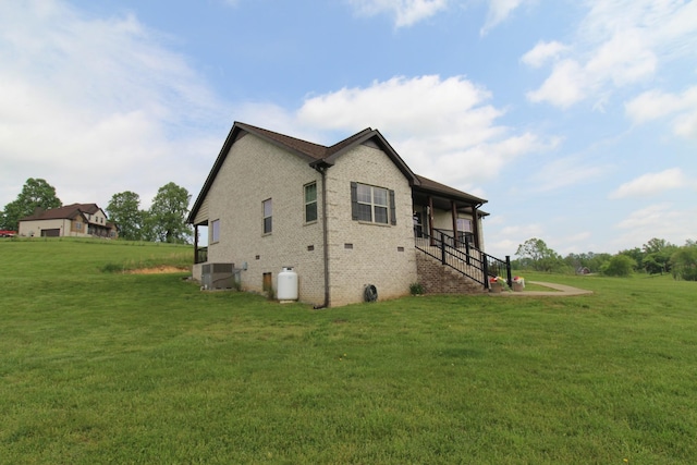 view of side of property with a yard, brick siding, cooling unit, and stairs