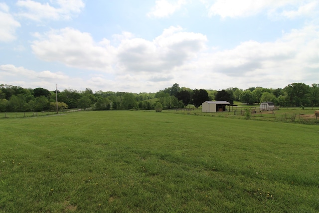 view of yard featuring a storage shed, a rural view, fence, and an outbuilding