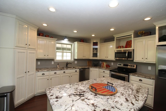 kitchen featuring open shelves, appliances with stainless steel finishes, a sink, dark wood finished floors, and a center island