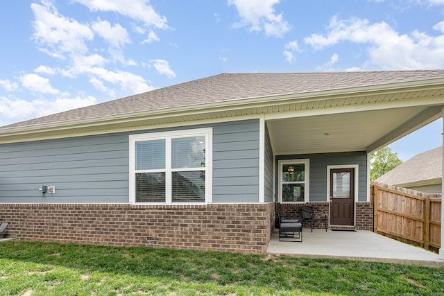 rear view of house featuring brick siding, fence, and a patio