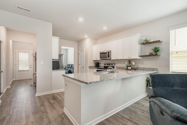 kitchen with a peninsula, appliances with stainless steel finishes, light wood-style flooring, and visible vents