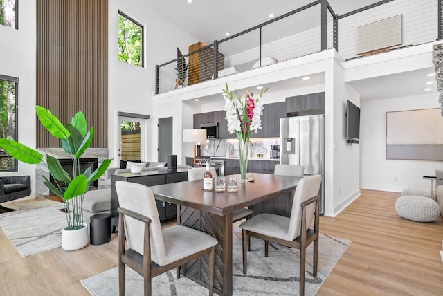 dining room with plenty of natural light, light wood-style floors, a towering ceiling, and baseboards
