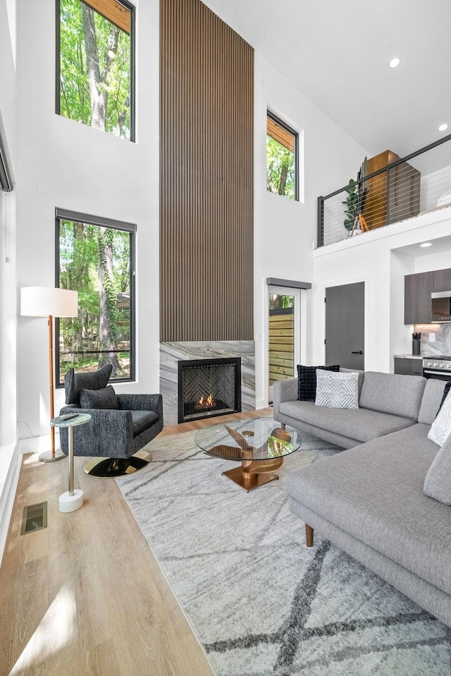 living room featuring visible vents, a towering ceiling, wood finished floors, a lit fireplace, and recessed lighting