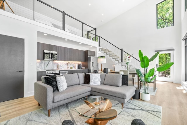 living area with stairs, recessed lighting, light wood-type flooring, and a towering ceiling