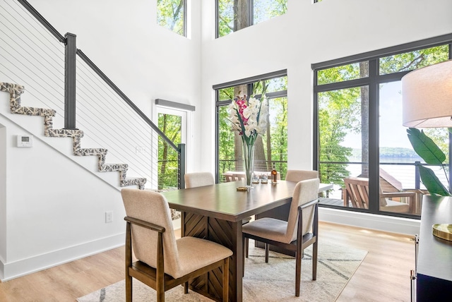 dining room featuring light wood-style flooring, a water view, a high ceiling, and a wealth of natural light