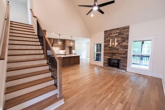 living area featuring a ceiling fan, a fireplace, high vaulted ceiling, light wood-style floors, and stairs