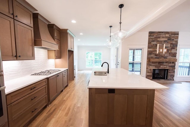 kitchen with custom range hood, a sink, light wood-style flooring, and stainless steel gas stovetop