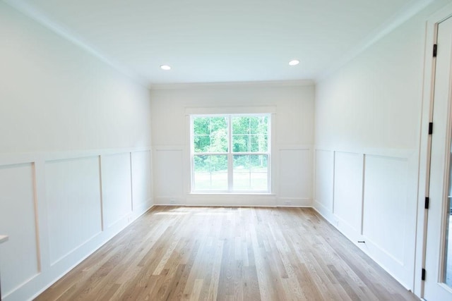 spare room with ornamental molding, wainscoting, a decorative wall, and light wood-style flooring