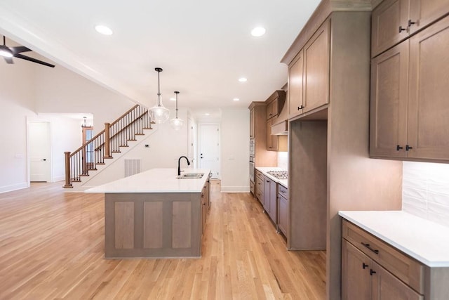 kitchen featuring a sink, light wood finished floors, light countertops, an island with sink, and backsplash